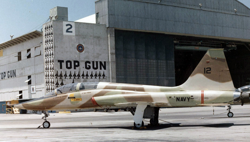 In den Anfangsjahren nutzte die „Top Gun“-Schule zweisitzige Überschalltrainer vom Typ Northrop DT-38 „Talon“ zur Feinddarstellung. Diese „Talon“ wurde 1974 in Miramar aufgenommen. Später trat die verbesserte Northrop F-5 „Tiger II“ an die Stelle der DT-38.  Die MiG-Silhouetten auf dem Hangar sollen über Vietnam abgeschossene Feindmaschinen darstellen. (#3)